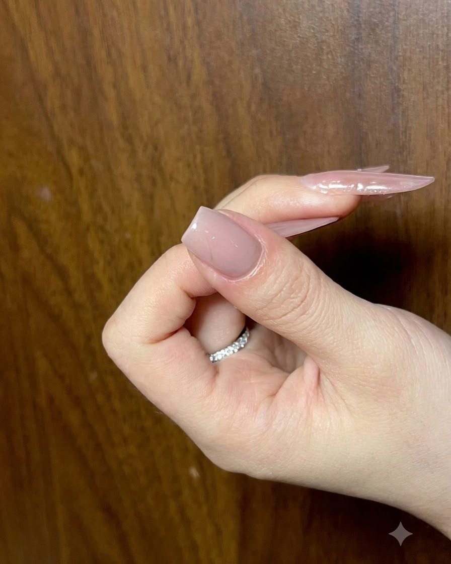 Una mano che tiene ununghia con uno strato di base nude completato, vista da unangolazione per controllare la levigatezza.