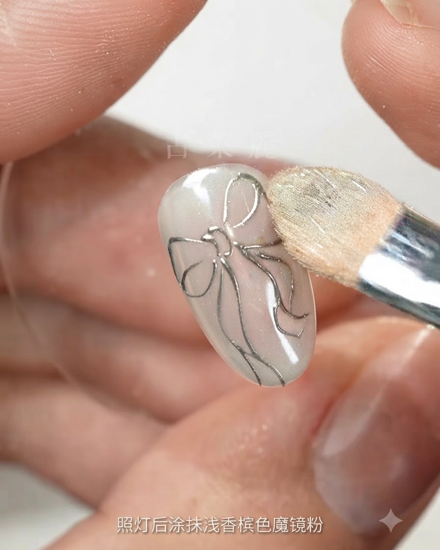 Una spugnetta per trucco che sfuma la polvere magica color champagne chiaro su un unghia con il contorno di un fiocco argentato.