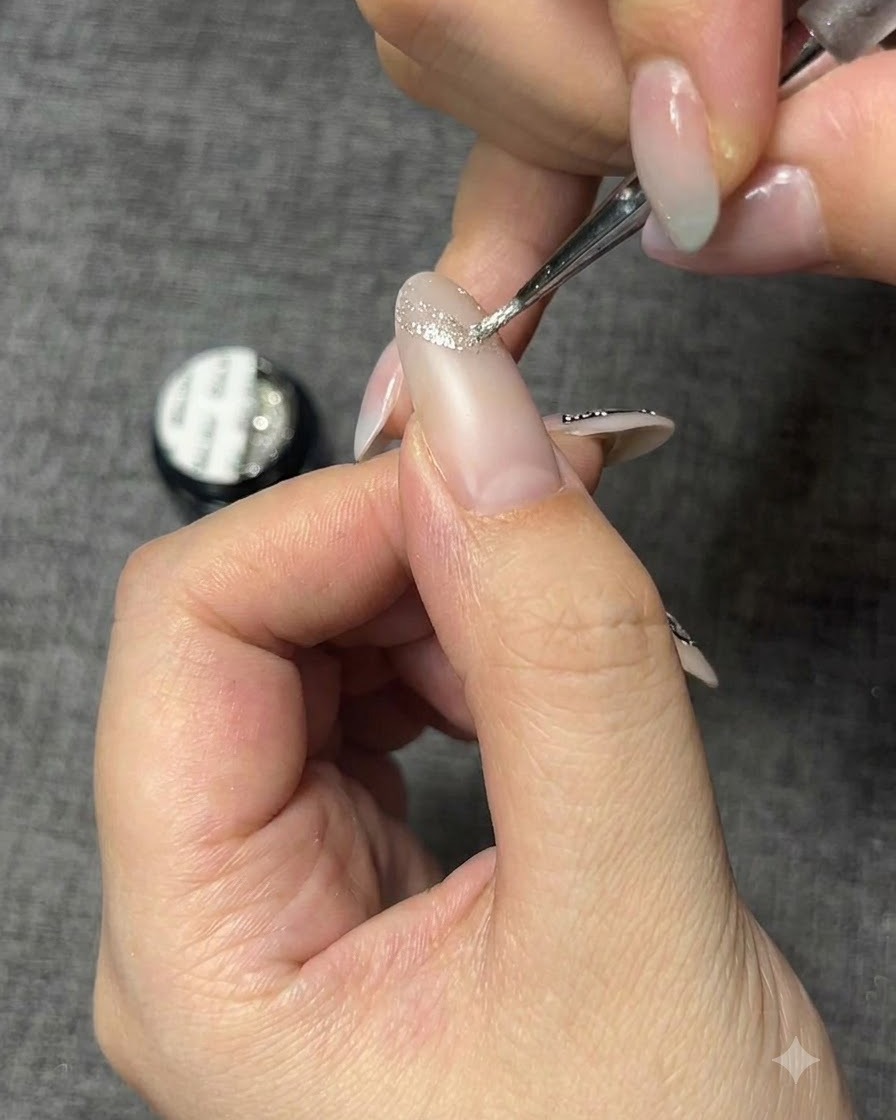 Un pennello di dettaglio fine applica un gel glitterato argentato per creare il contorno di una farfalla su ununghia.