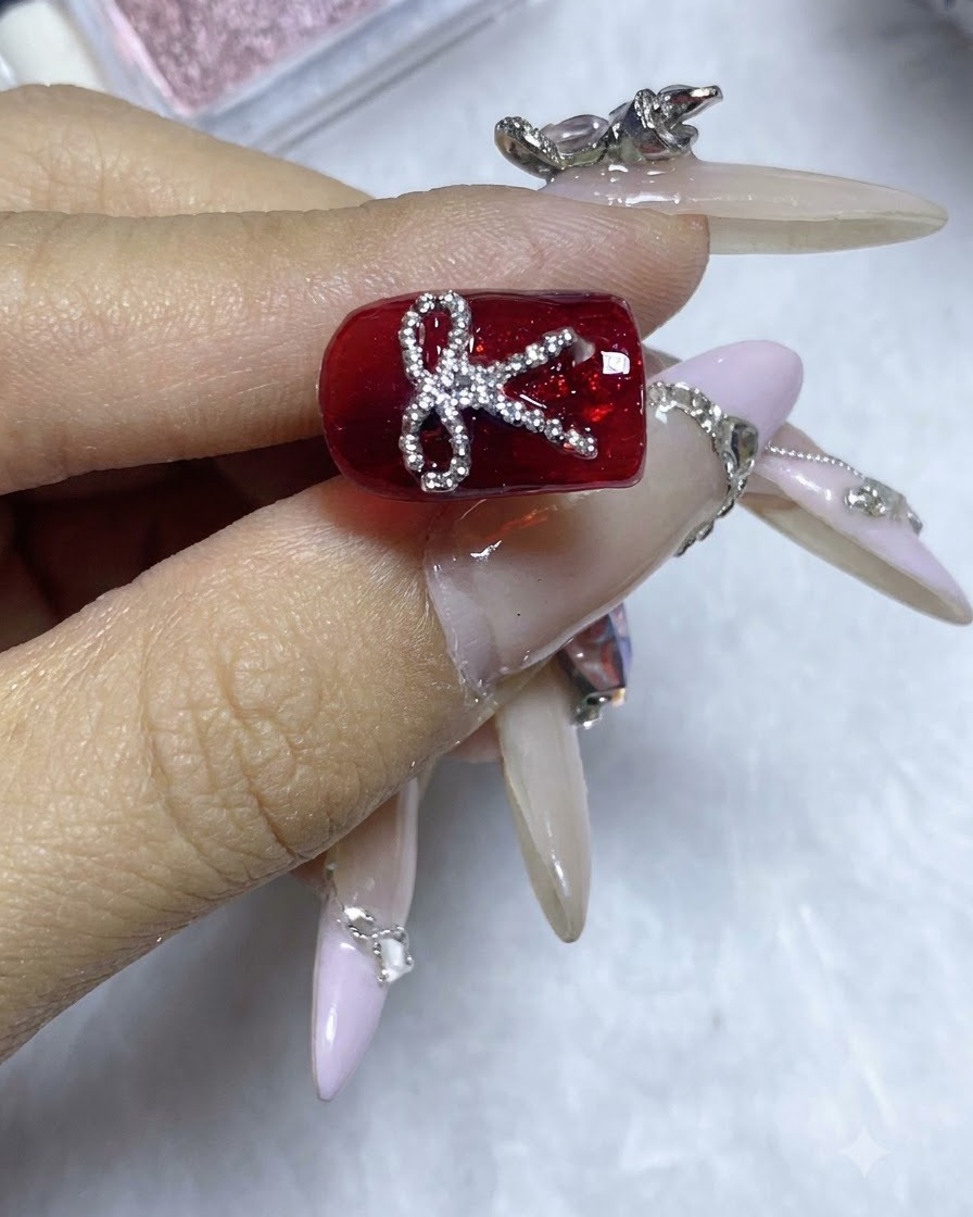 Un design di unghie rosse completato con un fiocco scintillante di sfere dacciaio sotto una brillante illuminazione da studio.