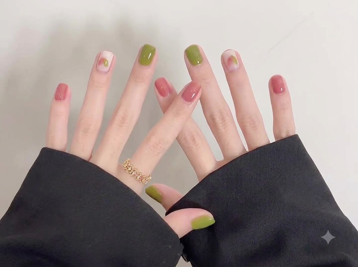 Dettaglio ravvicinato incentrato sulle unghie lucide verdi e rosa della mano destra con delicate decorazioni doodle.