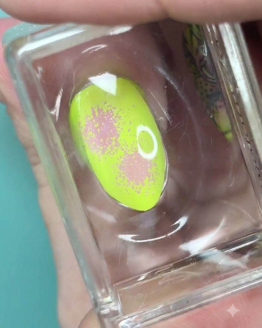 Un timbro in silicone trasparente che regge ununghia verde neon con una sfumatura rosa tenue e una tessitura puntinata.