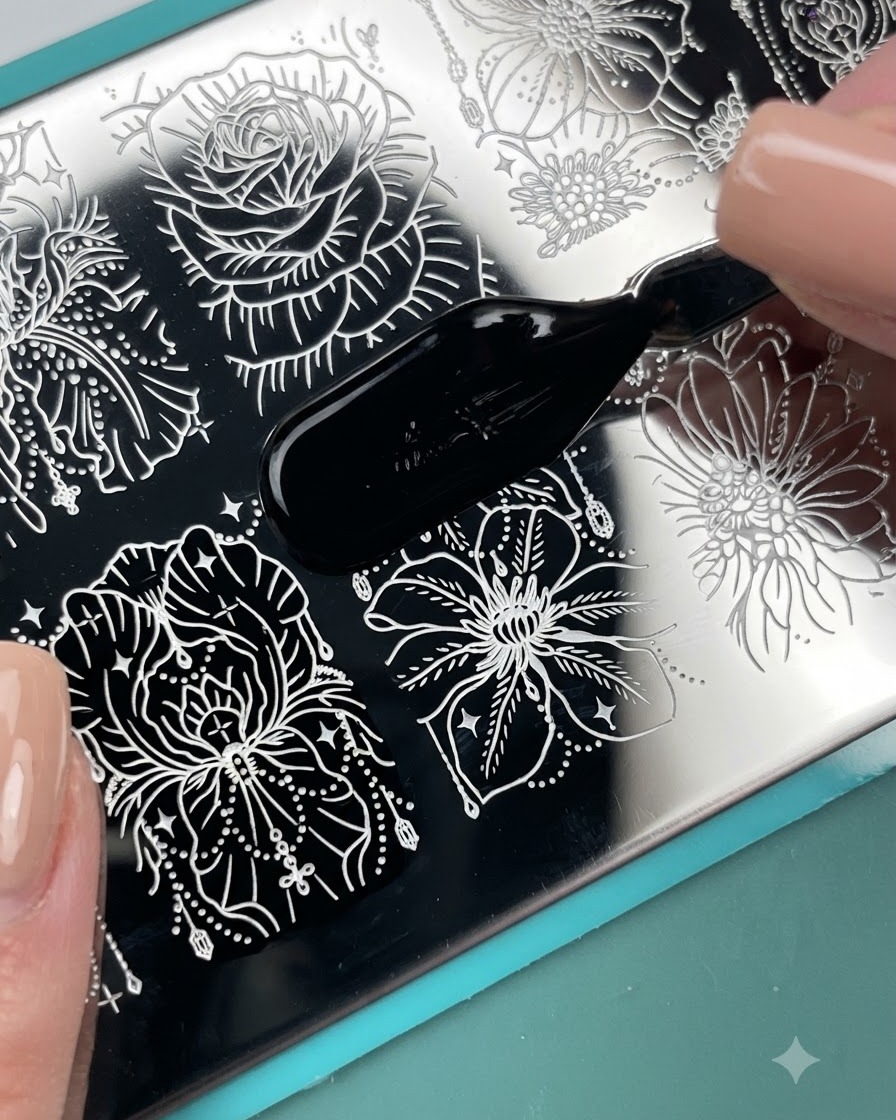 Un pennello applicatore che stende lo smalto da stamping nero su un motivo floreale inciso su una piastra metallica per stamping.