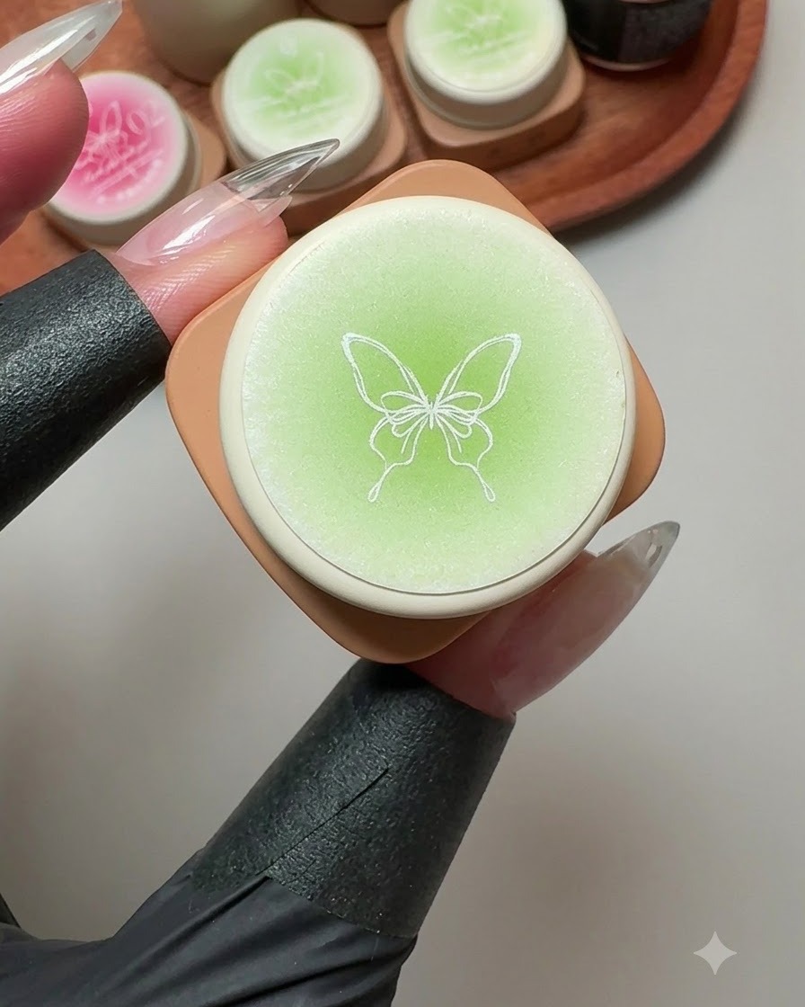 Un recipiente de gel sólido con una ilustración de mariposa en la tapa, rodeado de botes de gel verde y rosa.