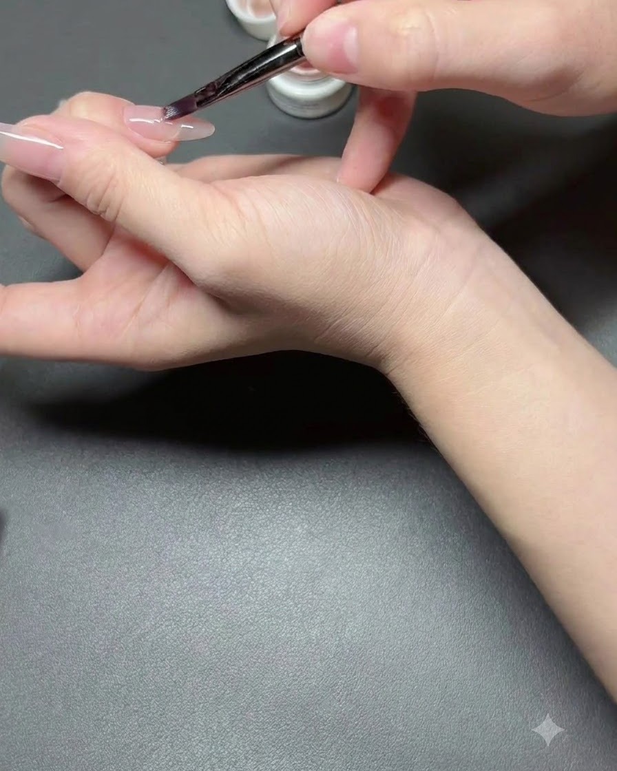 Un pennello per unghie che applica un sottile strato di smalto nude semi-trasparente su ununghia.