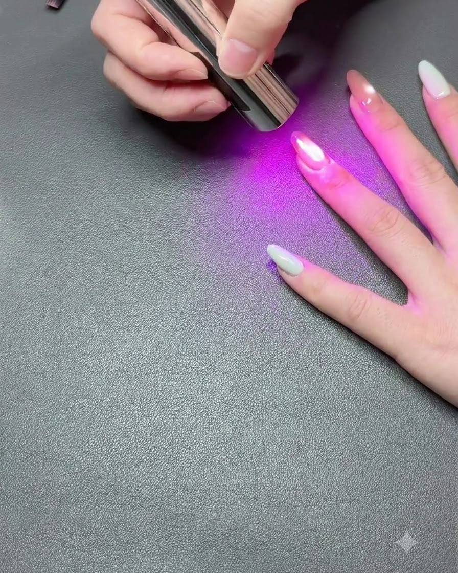 Una mano appoggiata su una superficie scura mentre una lampada UV portatile polimerizza lo smalto gel cat-eye.