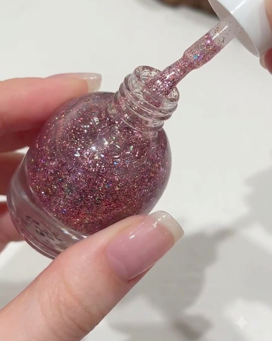 Una mano che svita il tappo bianco di un flacone di smalto Orange, sollevando un pennello gocciolante di gel glitter rosa.