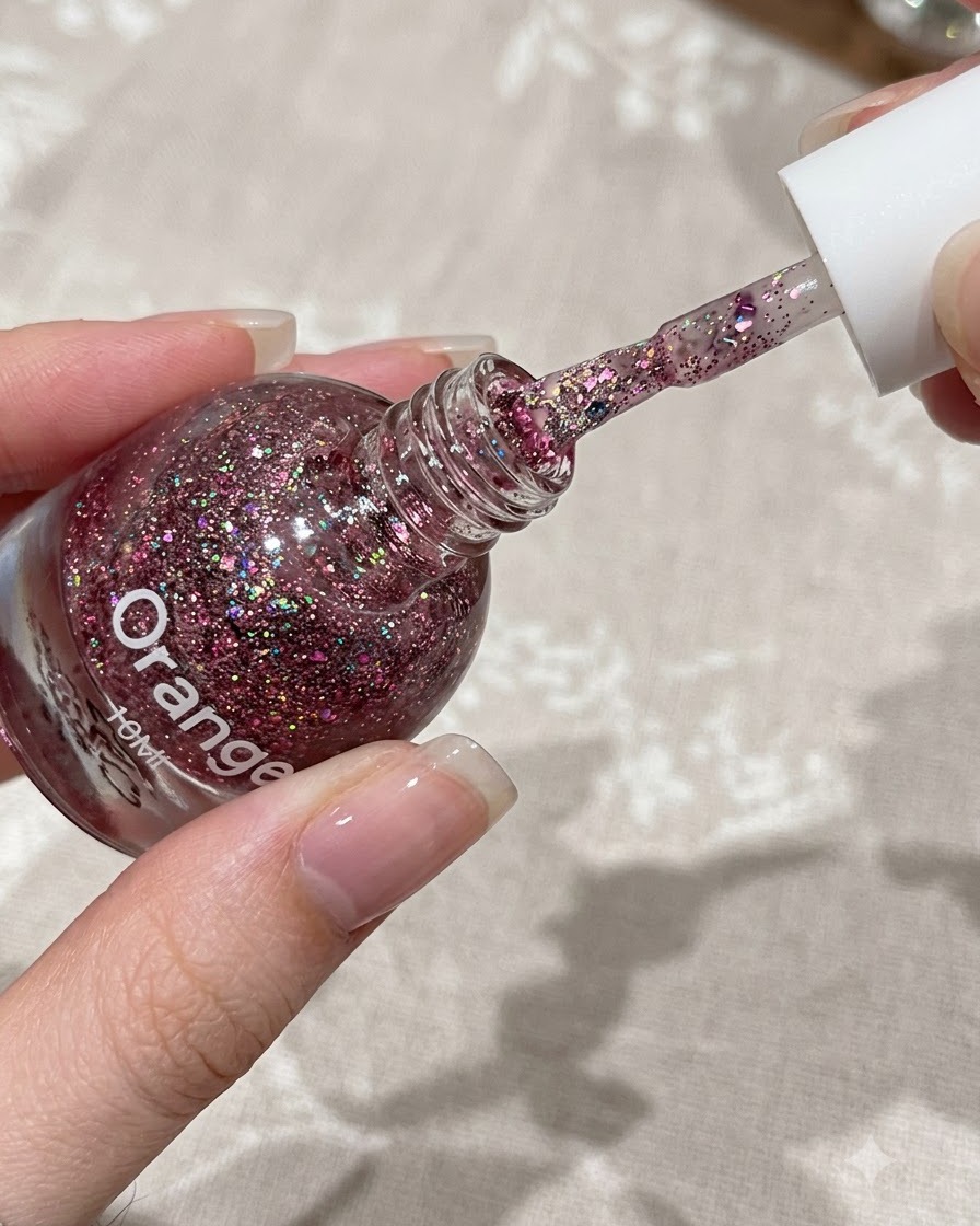 Un pennello che applica un sottile strato di gel glitter rosa sulla metà superiore di ununghia naturale.