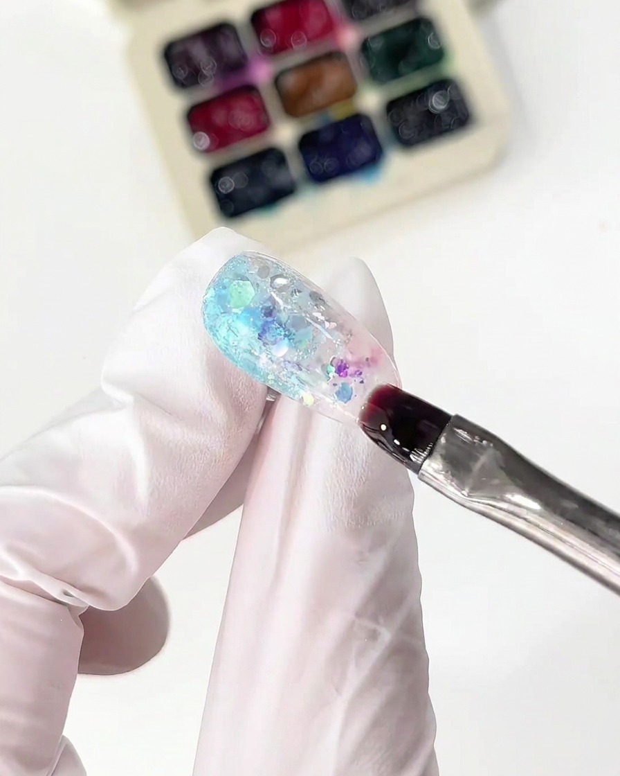 Un pennello sottile applica il glass gel rosa accanto alla sezione blu su ununghia.