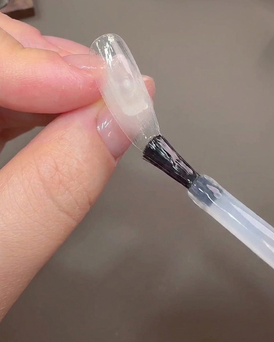 Un pennello per unghie applica il gel costruttore su un tip trasparente per coprire la linea di crescita.