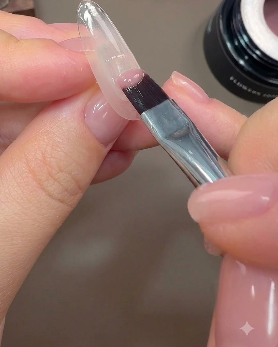 Un pennello per unghie applica una copertura a metà di gel colorato rosa nude sul bordo posteriore di ununghia.