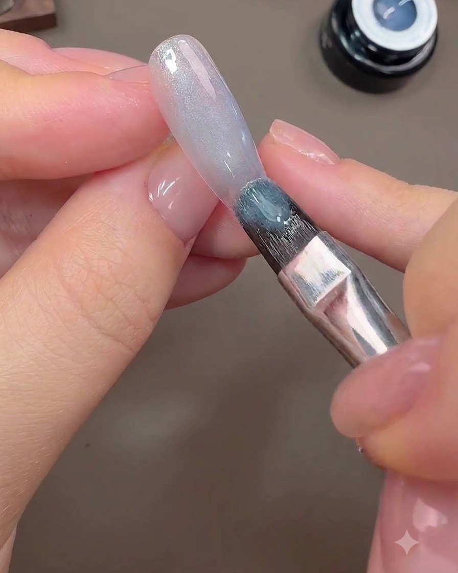Un pennello applica il gel cat-eye grigio-blu sulla superficie dellunghia per formare lo sfondo galattico.