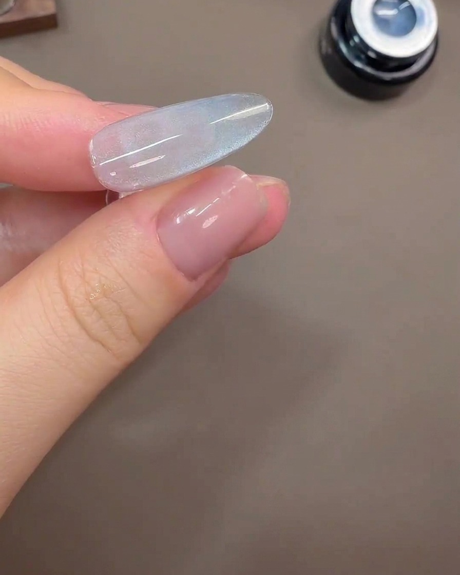 Ununghia che mostra un ampio riflesso di luce cat-eye su uno sfondo in gel grigio-blu.