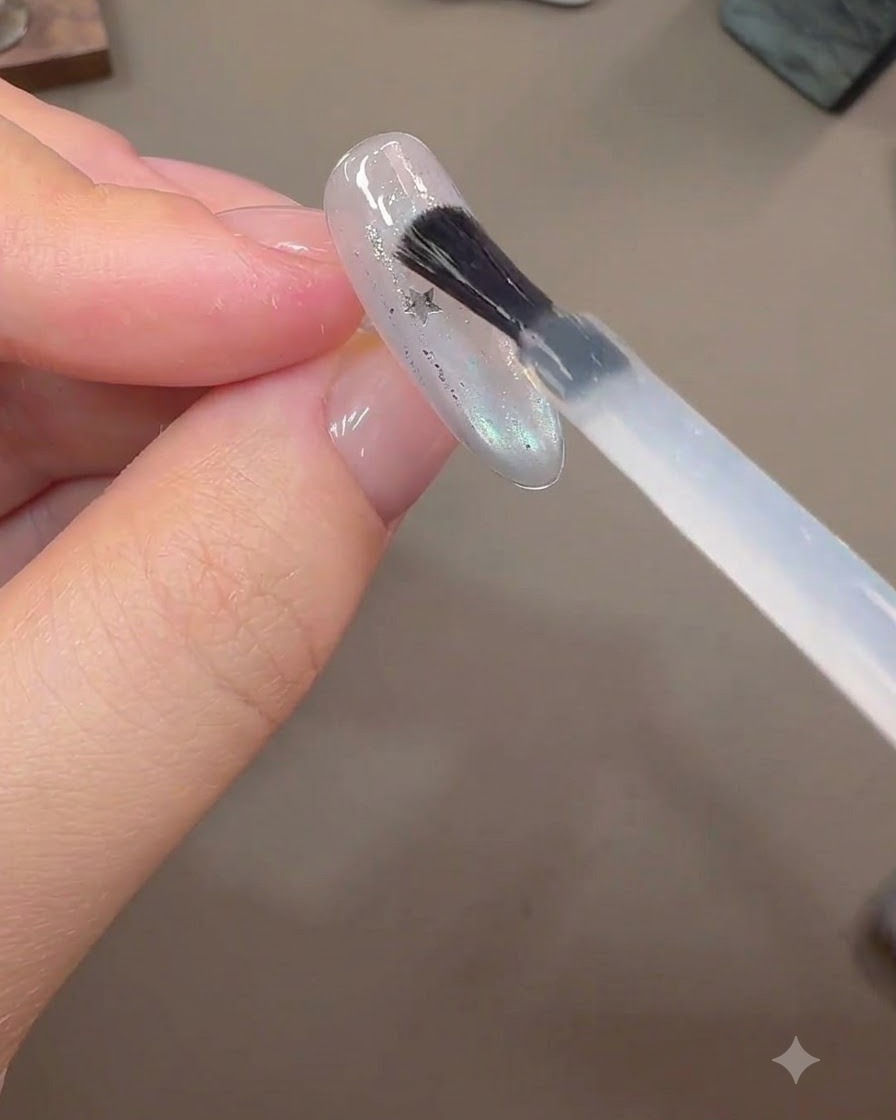 Un pennello applica uno spesso strato di gel costruttore sopra i pezzi di glitter a stella incorporati su unestensione ungueale finita.
