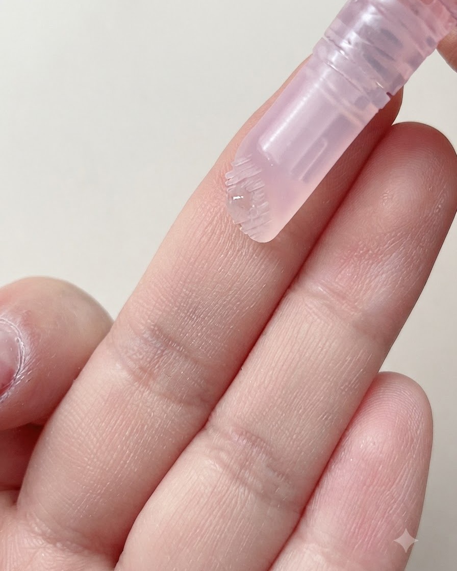 La testina con setole morbide di una penna per cuticole che eroga una goccia di siero idratante su un dito.