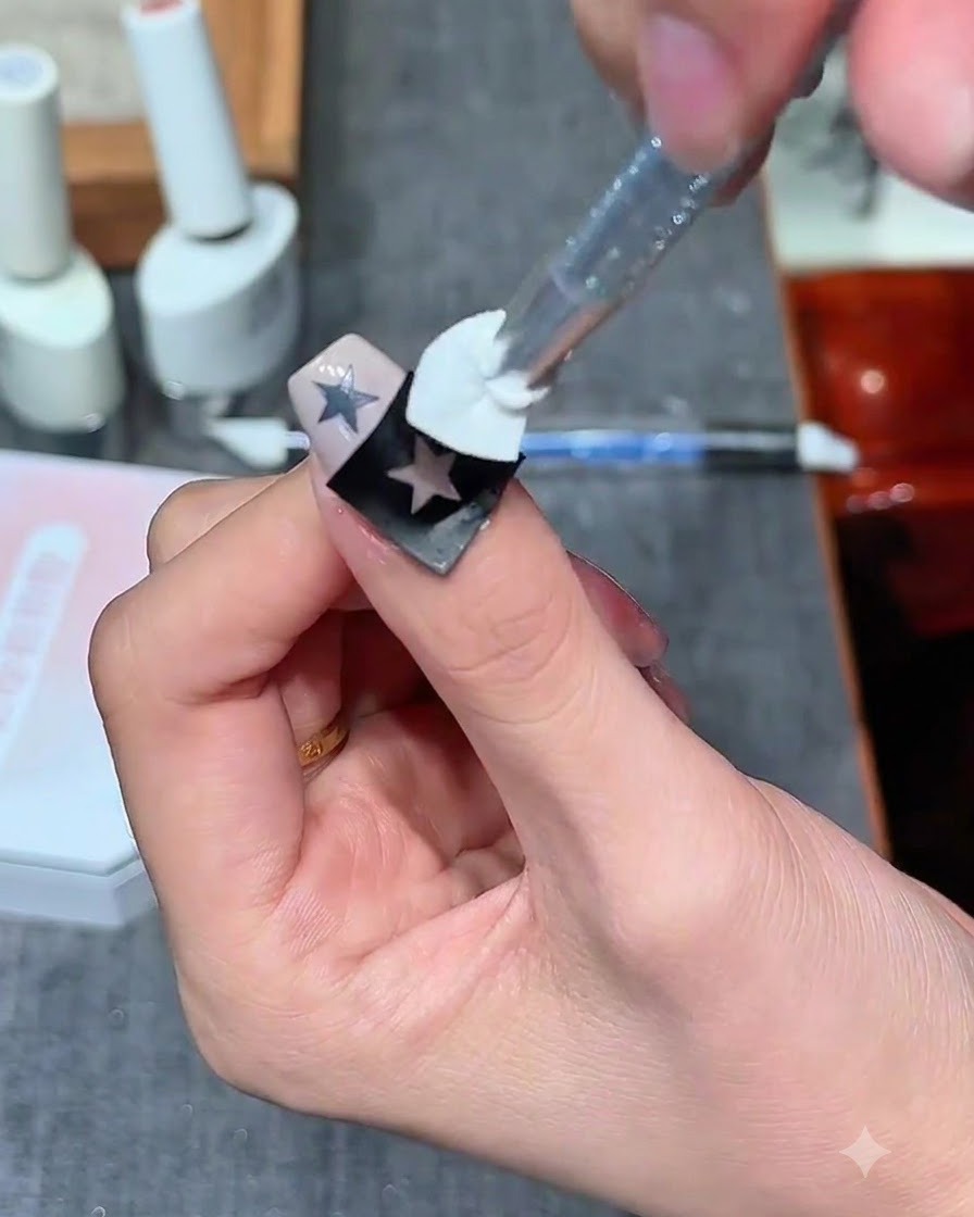 Un timbro a spugna applica gel bianco lattiginoso sopra un adesivo con contorno di stella vuota su ununghia.