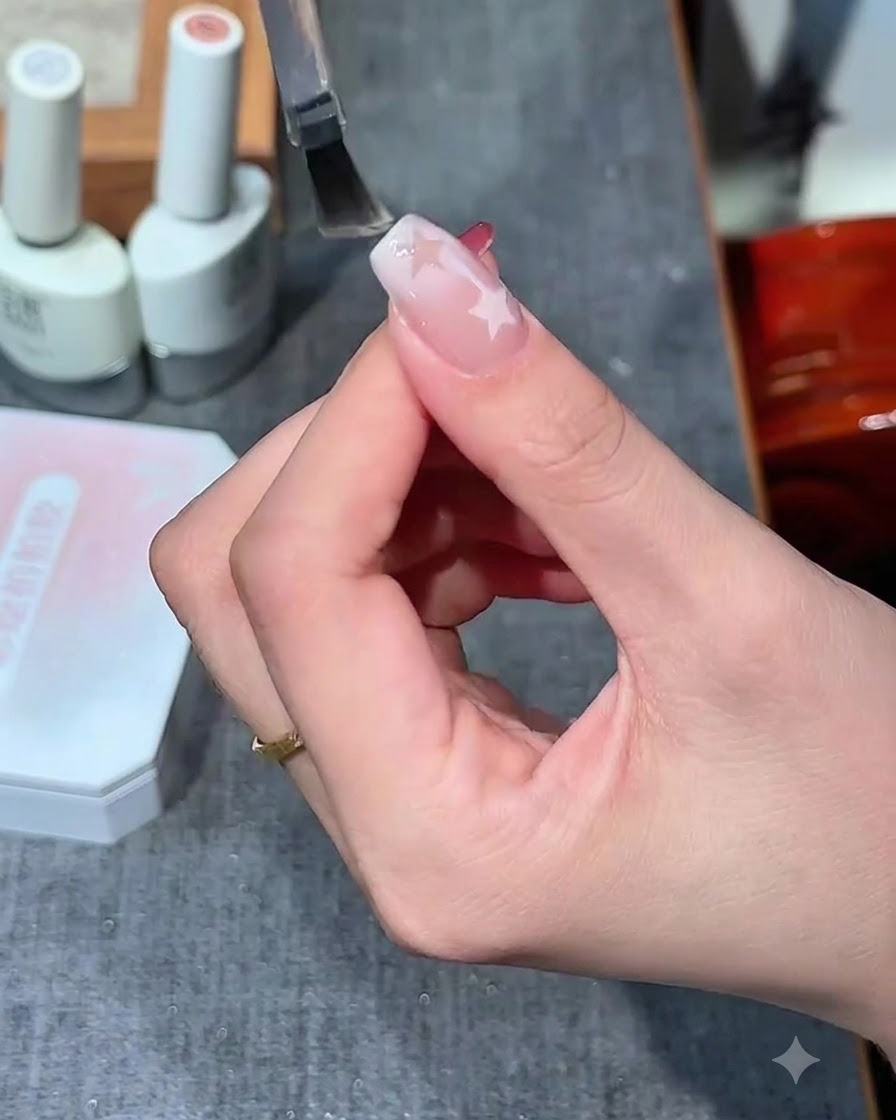 Un pennello per unghie applica un top coat trasparente e lucido su un design per unghie con motivo a stella.