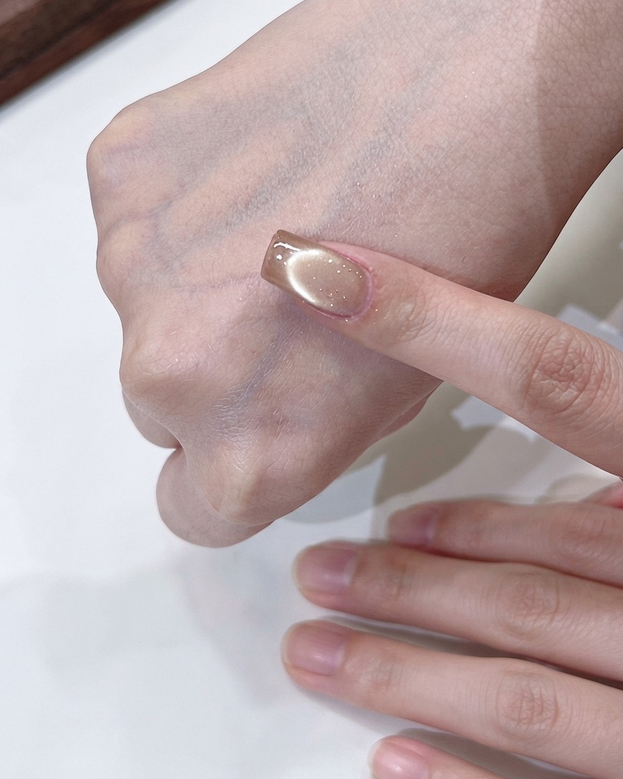 Una mano che tiene un magnete che compie movimenti circolari sopra ununghia cat-eye oro champagne per formare un effetto di luce fluida.