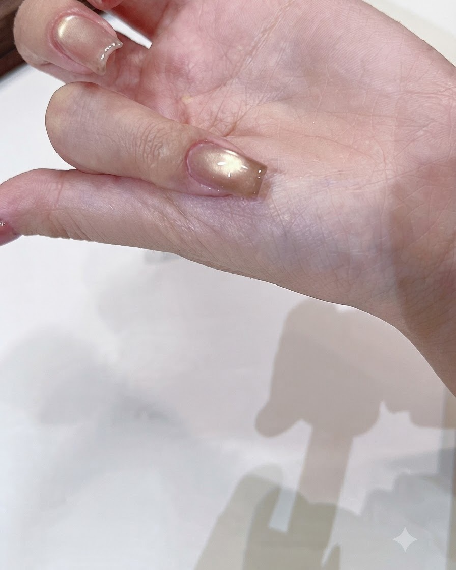 Un pennello che applica un top coat trasparente e lucido su ununghia cat-eye oro champagne polimerizzata.