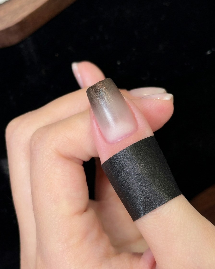 Ununghia posizionata sotto una piccola lampada UV/LED portatile per polimerizzare il primo strato sfumato di nero appena applicato.