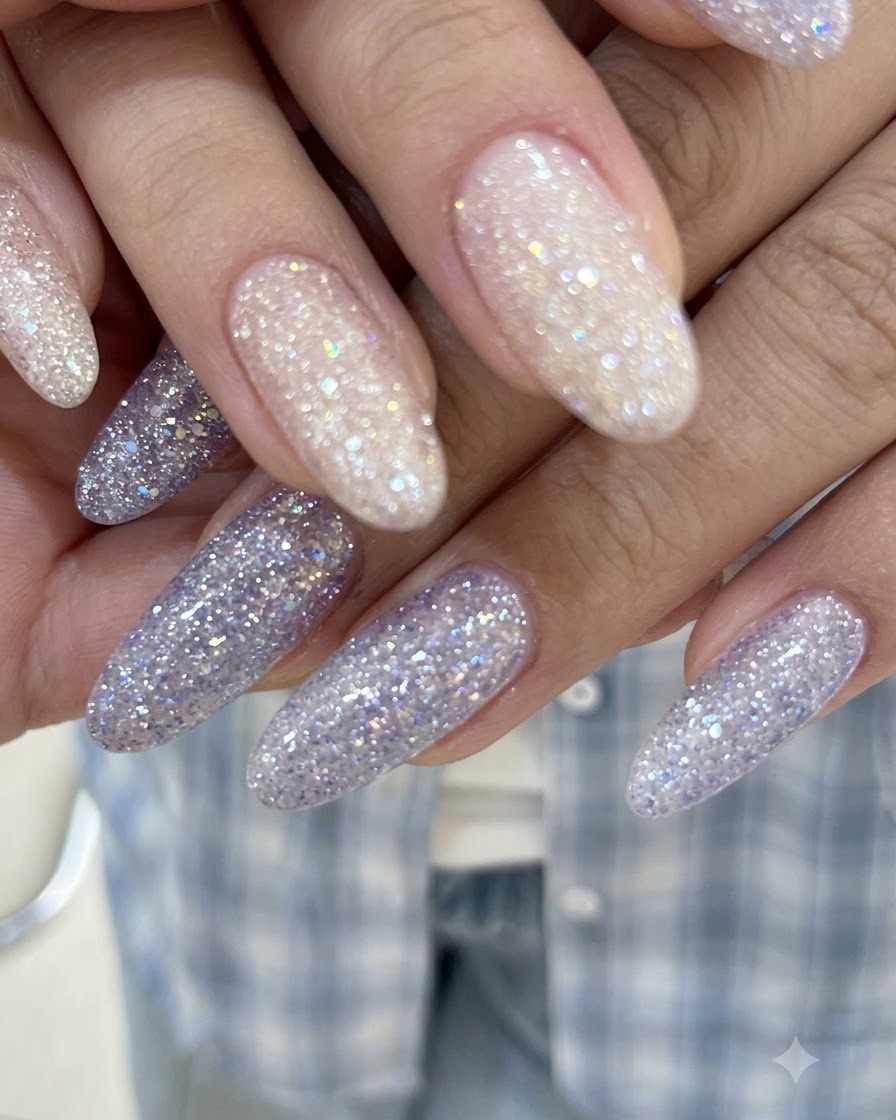Primo piano di mani con dita intrecciate che mostrano unghie in gel con glitter rosa nude e viola lucidi.