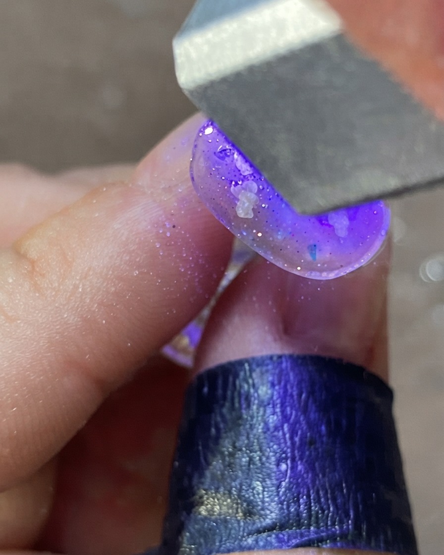 Una mano sotto una lampada per unghie UV/LED viola che polimerizza un design per unghie decorato.