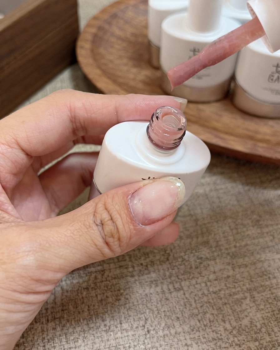 Un pennello applicatore con smalto gel nude rosa pesca miele tenuto sopra una boccetta aperta.
