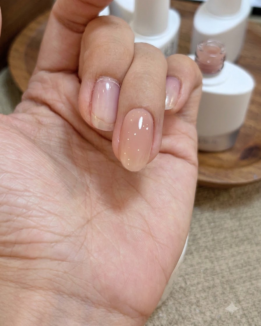 Una vista ravvicinata di una mano con uno strato lucido e bagnato di gel base trasparente applicato sopra lunghia rosa nude.