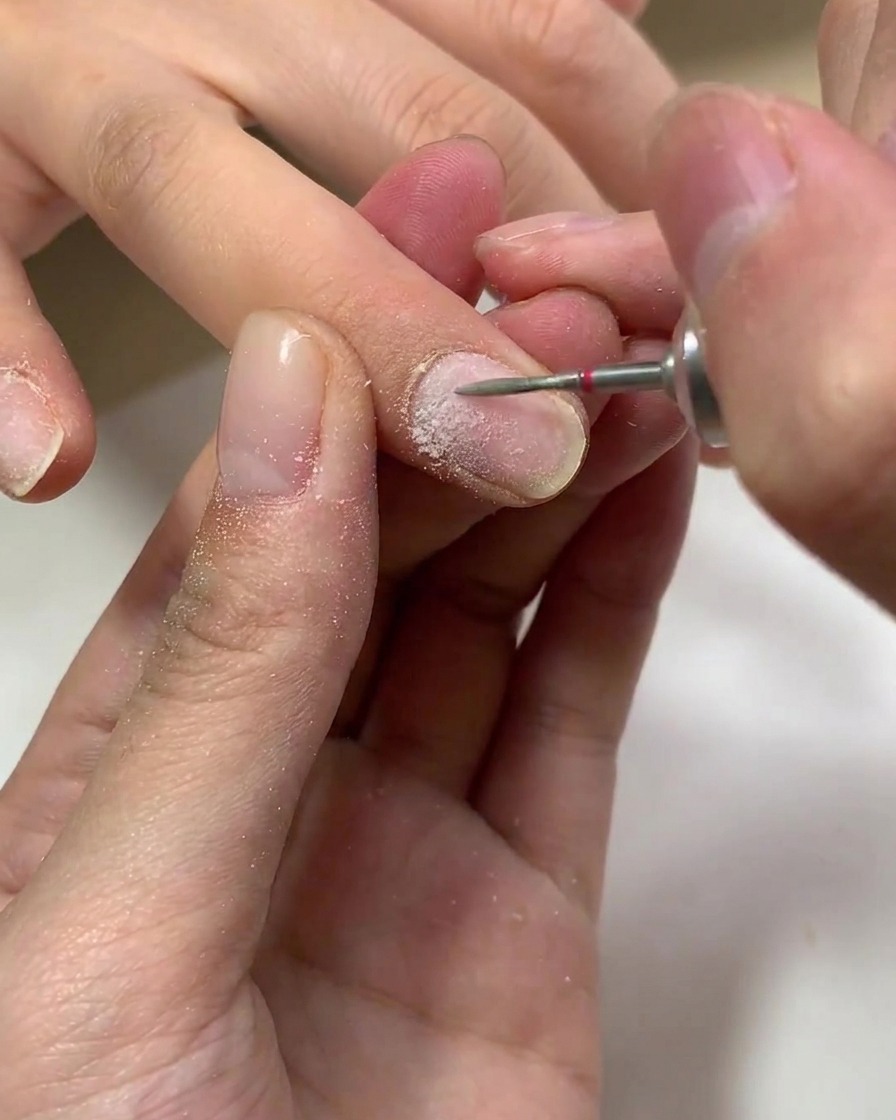 Un pennello che applica uno strato trasparente di base coat in gel su ununghia naturale.