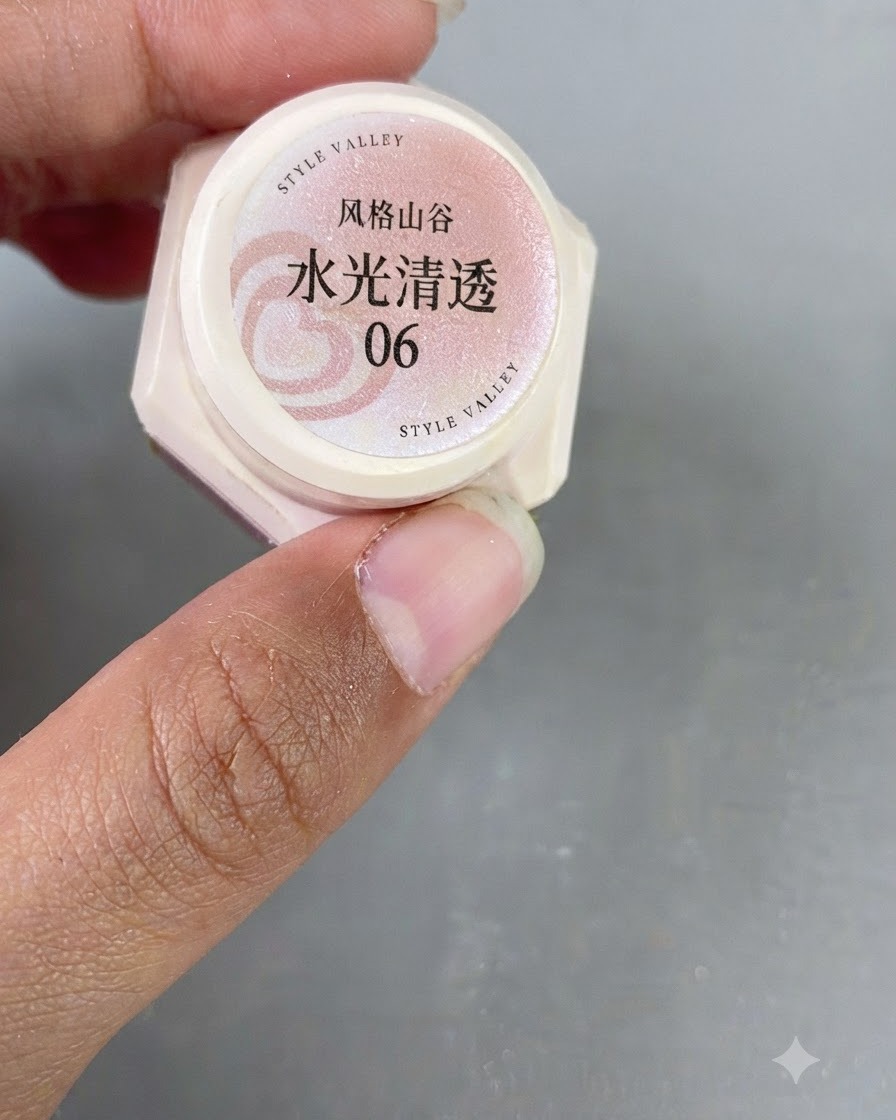 Primo piano di una mano che tiene un piccolo barattolo di gel cat-eye rosa traslucido etichettato con il numero 06.
