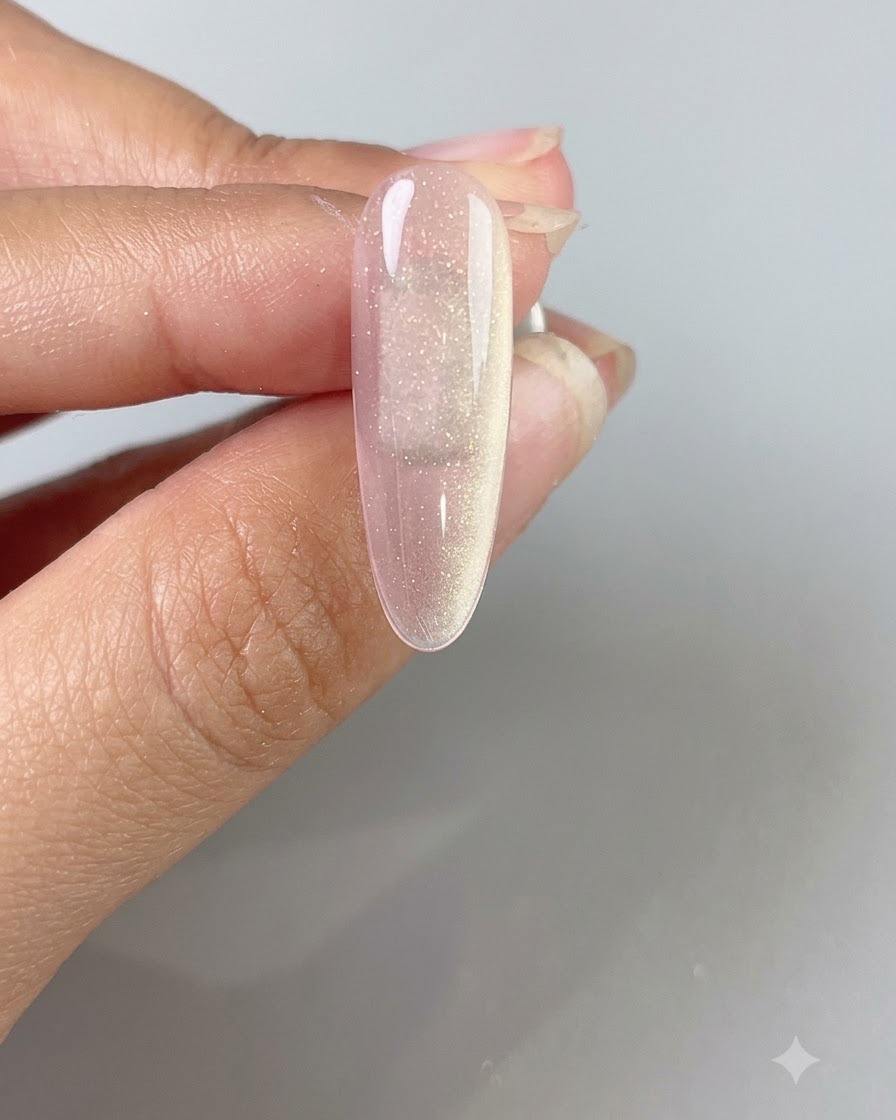 Una mano che tiene una bacchetta magnetica sopra ununghia in gel cat-eye rosa traslucido per creare un ampio fascio di luce luminoso.