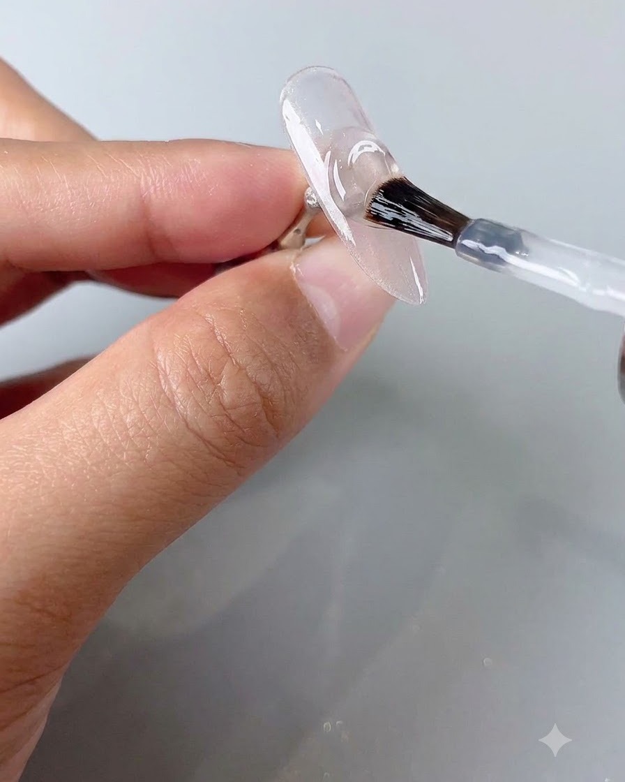 Un pennello per unghie che applica uno strato di top coat trasparente su ununghia cat-eye polimerizzata.