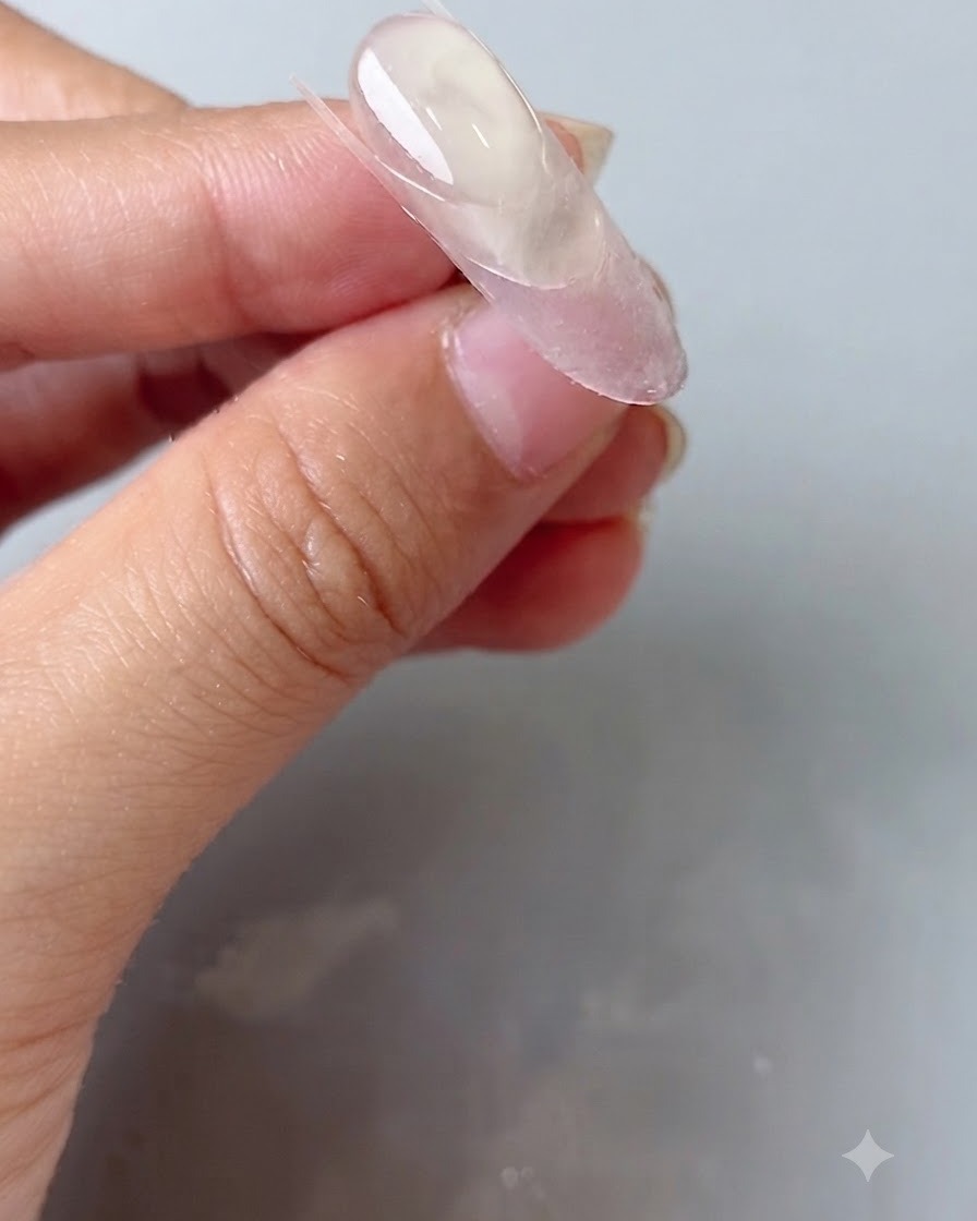 Uno strumento in silicone per unghie che preme un adesivo guida trasparente su ununghia ovale.