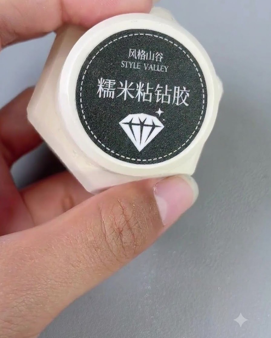 Un piccolo contenitore di gel diamantato adesivo Style Valley tenuto in mano accanto a un pennello per unghie.