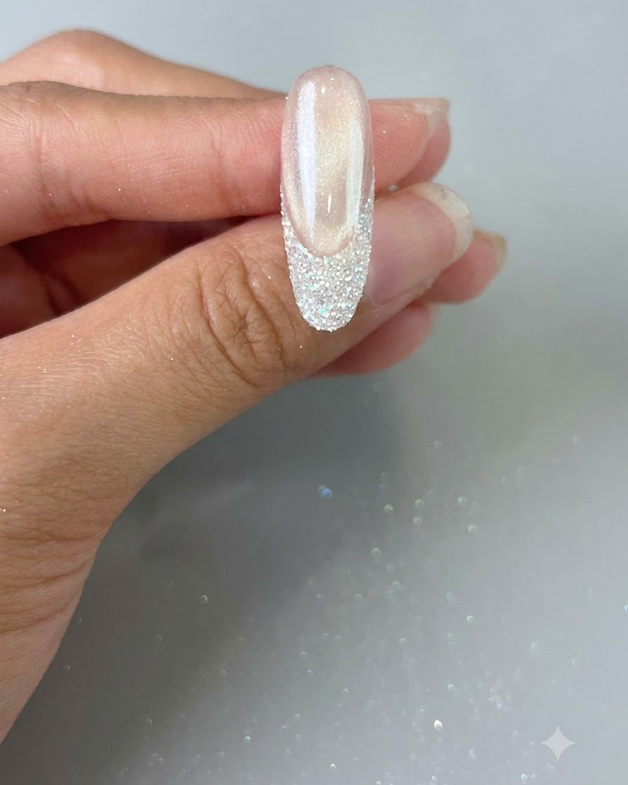 Una mano che regge ununghia finita con una punta French glitterata, pronta per la polimerizzazione finale.