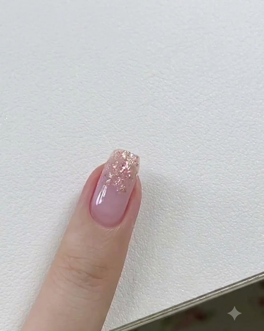 Un pennello per gel applica un sottile strato di builder gel trasparente su ununghia con accenti glitter.