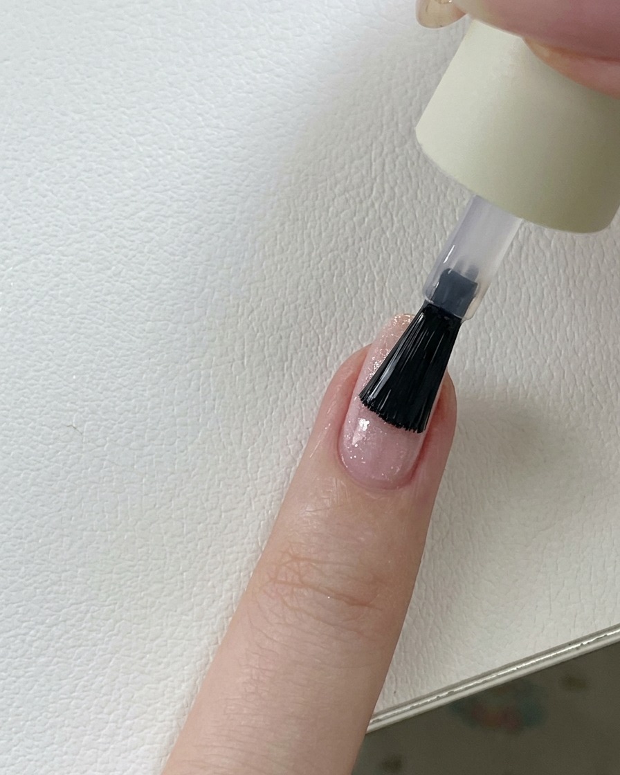 Un pennello che applica un top coat trasparente e lucido sopra ununghia in gel con glitter rosa.