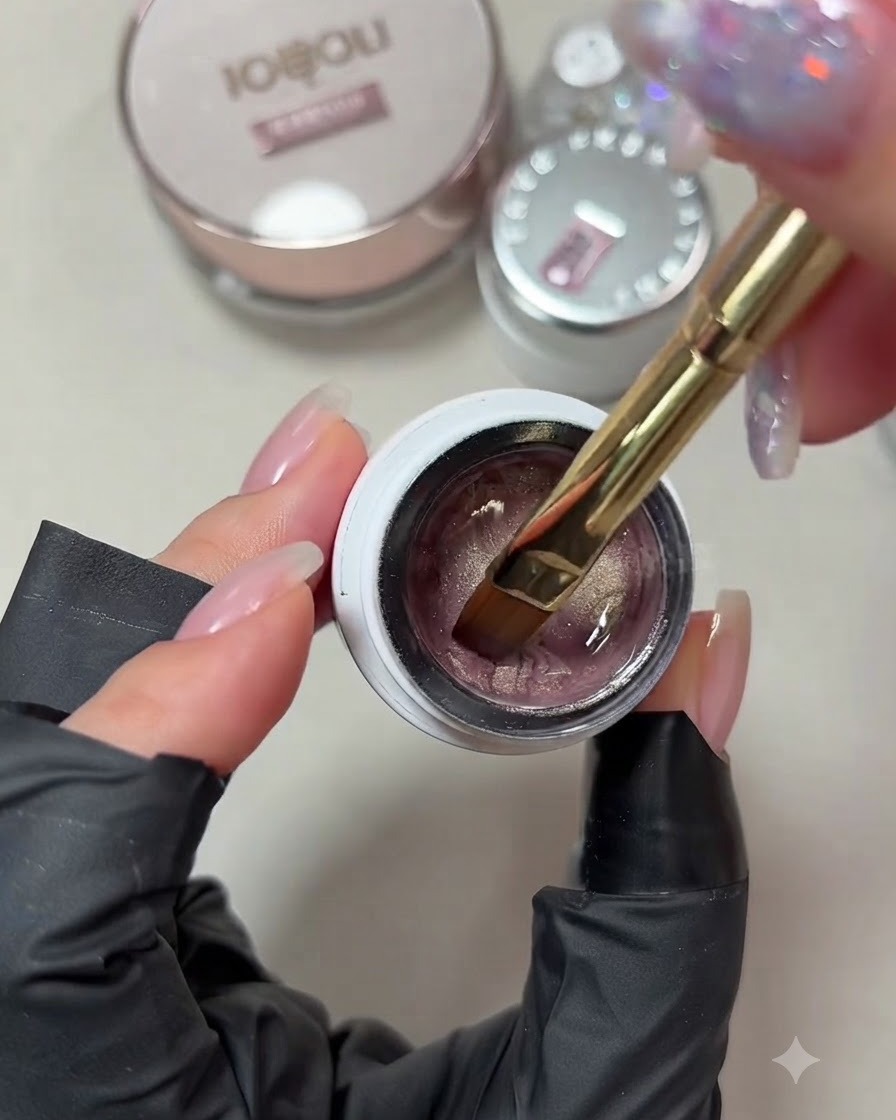 Una vista ravvicinata di un pennello da gel che si intinge in un vasetto di smalto gel cat-eye rosa champagne tenue.