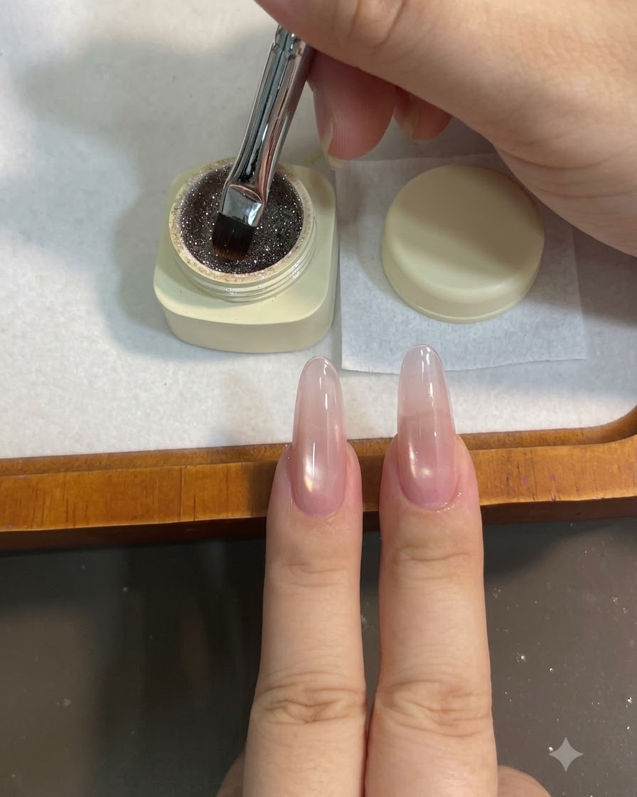 Un pennello piatto per gel che preleva da un vasetto di gel glitterato color caffè.