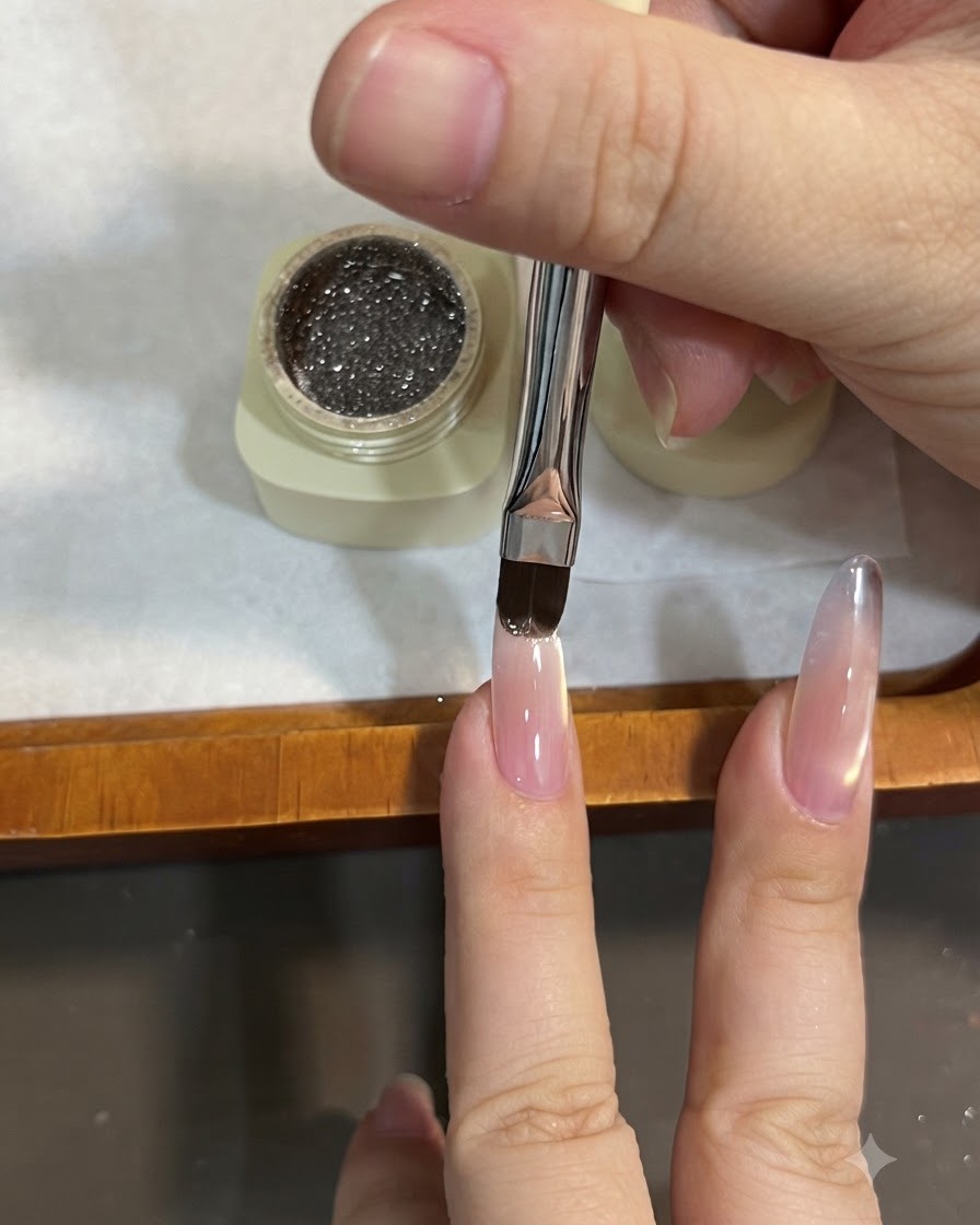 Un pennello piatto applica il gel glitterato sulla punta di ununghia a mandorla, tirandolo verso il basso per creare leffetto ombré.