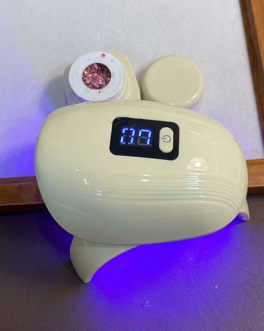 Una mano posiziona le dita sotto una lampada LED per unghie compatta blu e bianca.