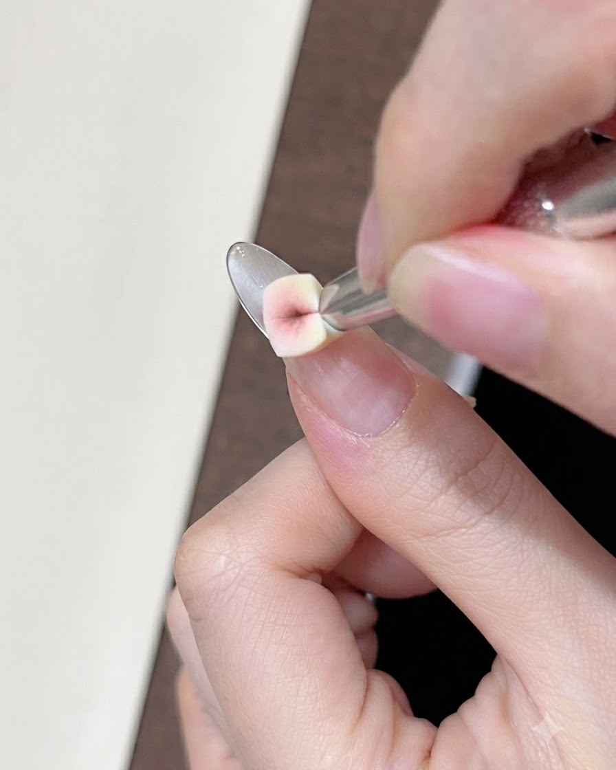 Un primo piano di una piccola spugnetta a cuneo che tampona il gel correttore nude sullunghia naturale vicino alla linea del sorriso.