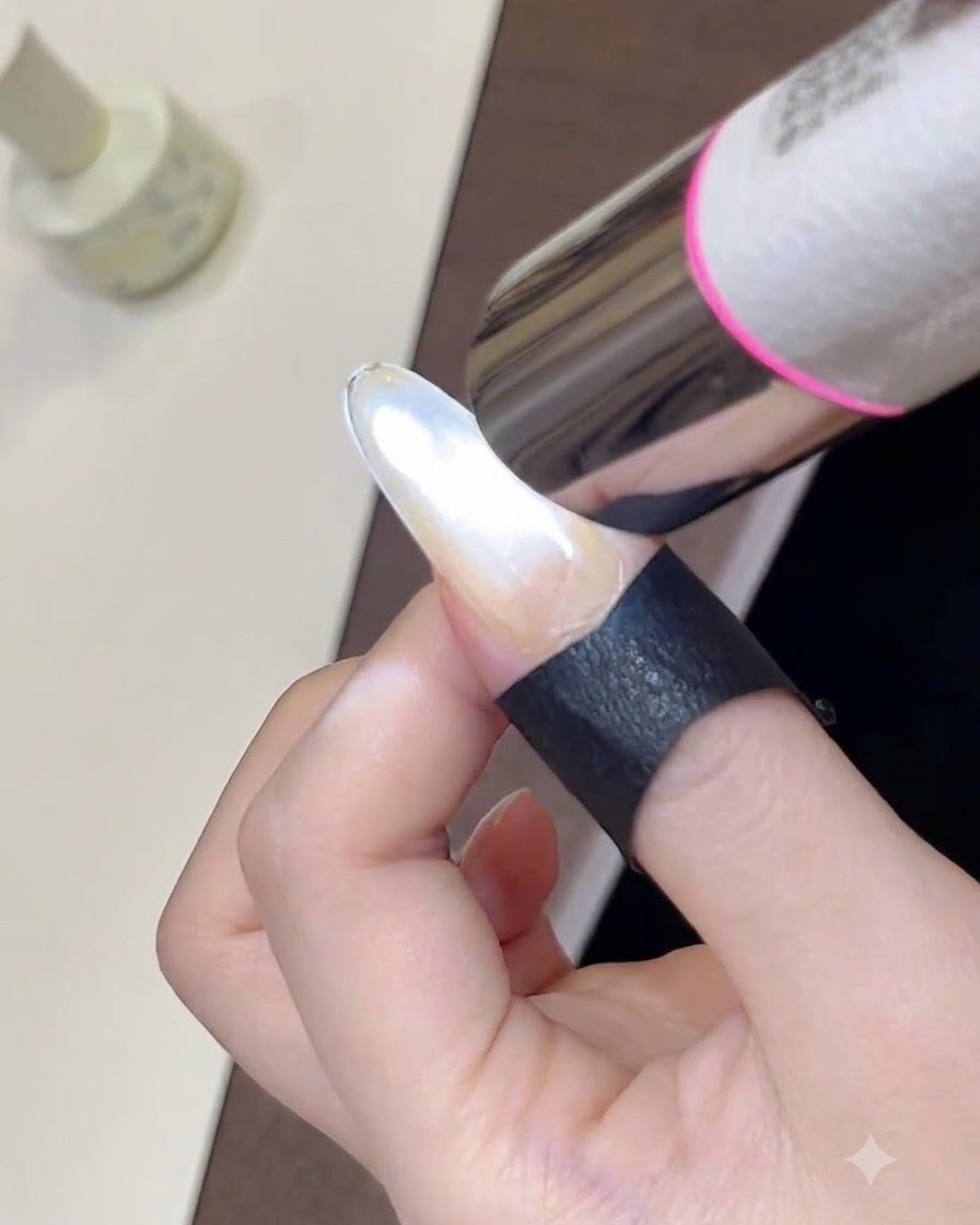 Un primo piano di una mini lampada UV portatile che polimerizza uno smalto gel cat-eye appena modellato su ununghia.