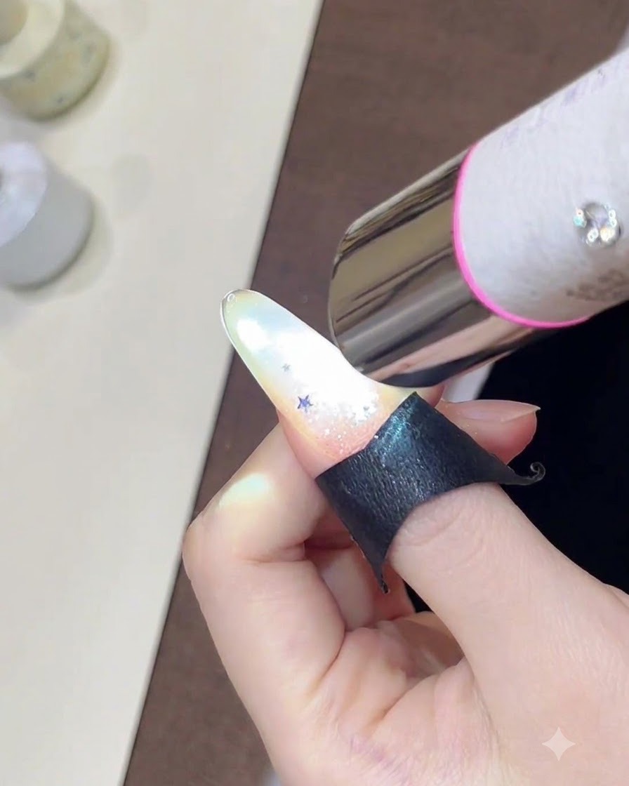 Una mano che tiene una mini lampada UV su ununghia decorata con una scintillante sfumatura glitterata e piccole paillettes a stella.