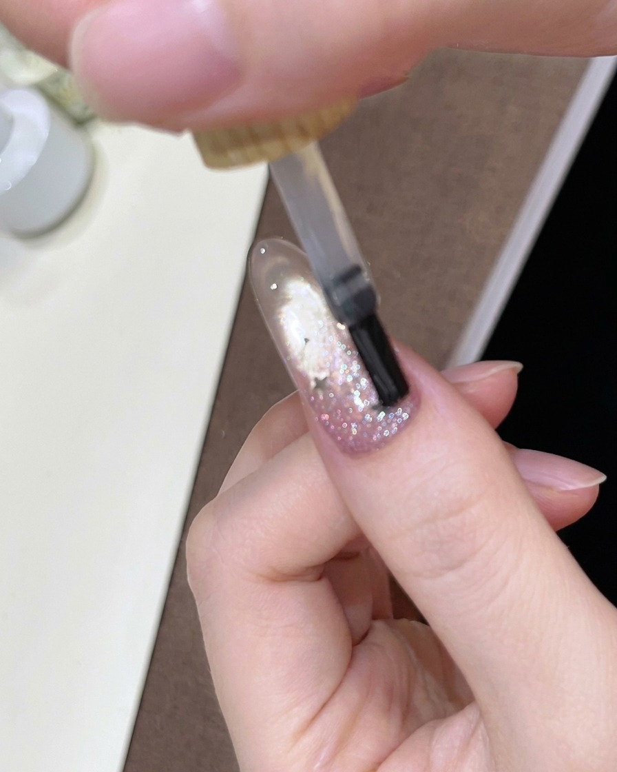 Un pennello che applica un top coat trasparente e lucido sullunghia sfumata decorata.