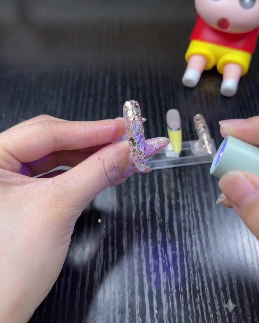 Una mano che tiene una mini lampada UV/LED portatile sopra ununghia glitterata per polimerizzare il gel.