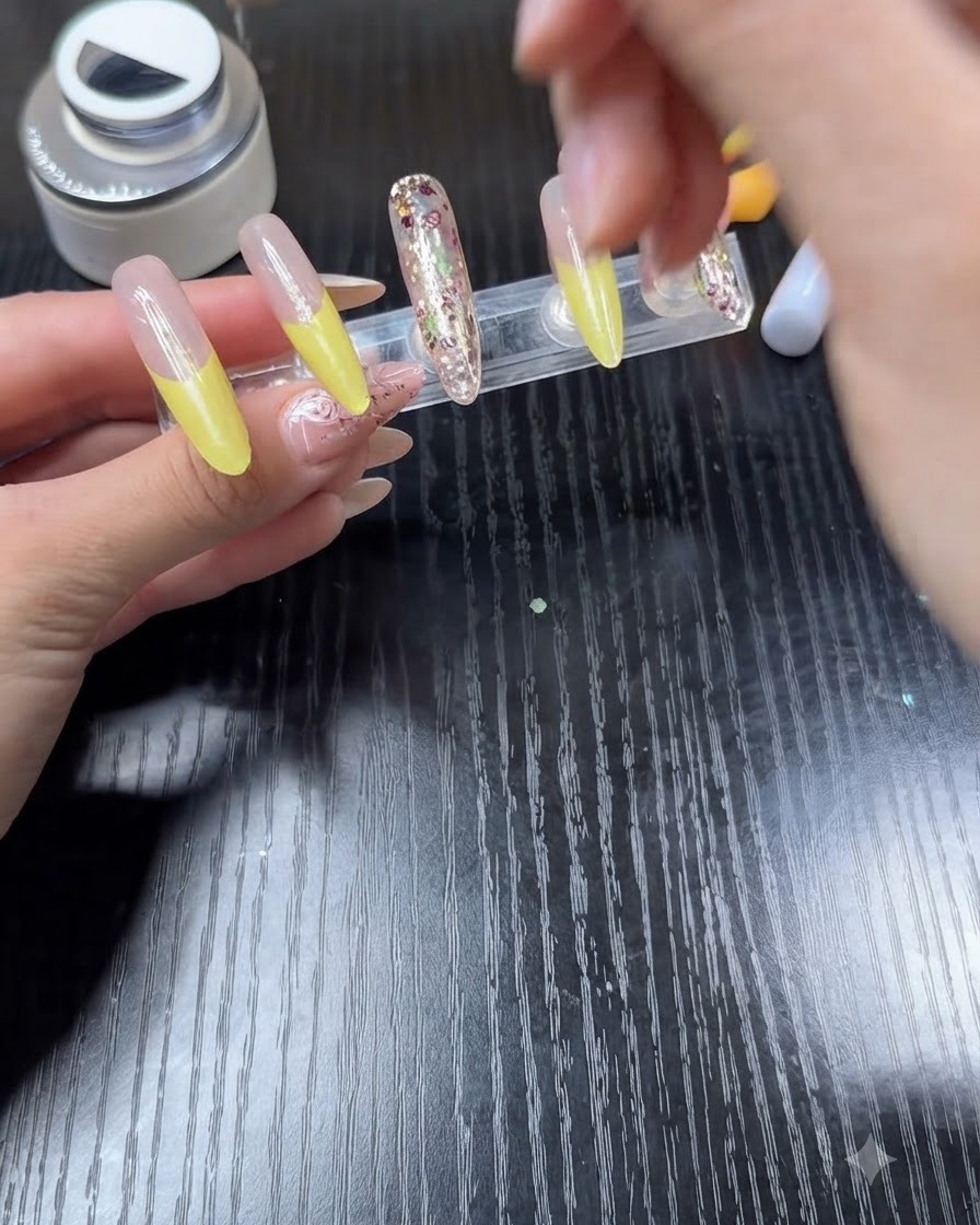 Un pennello da smalto che applica il top coat trasparente su ununghia caratterizzata da una French gialla brillante.