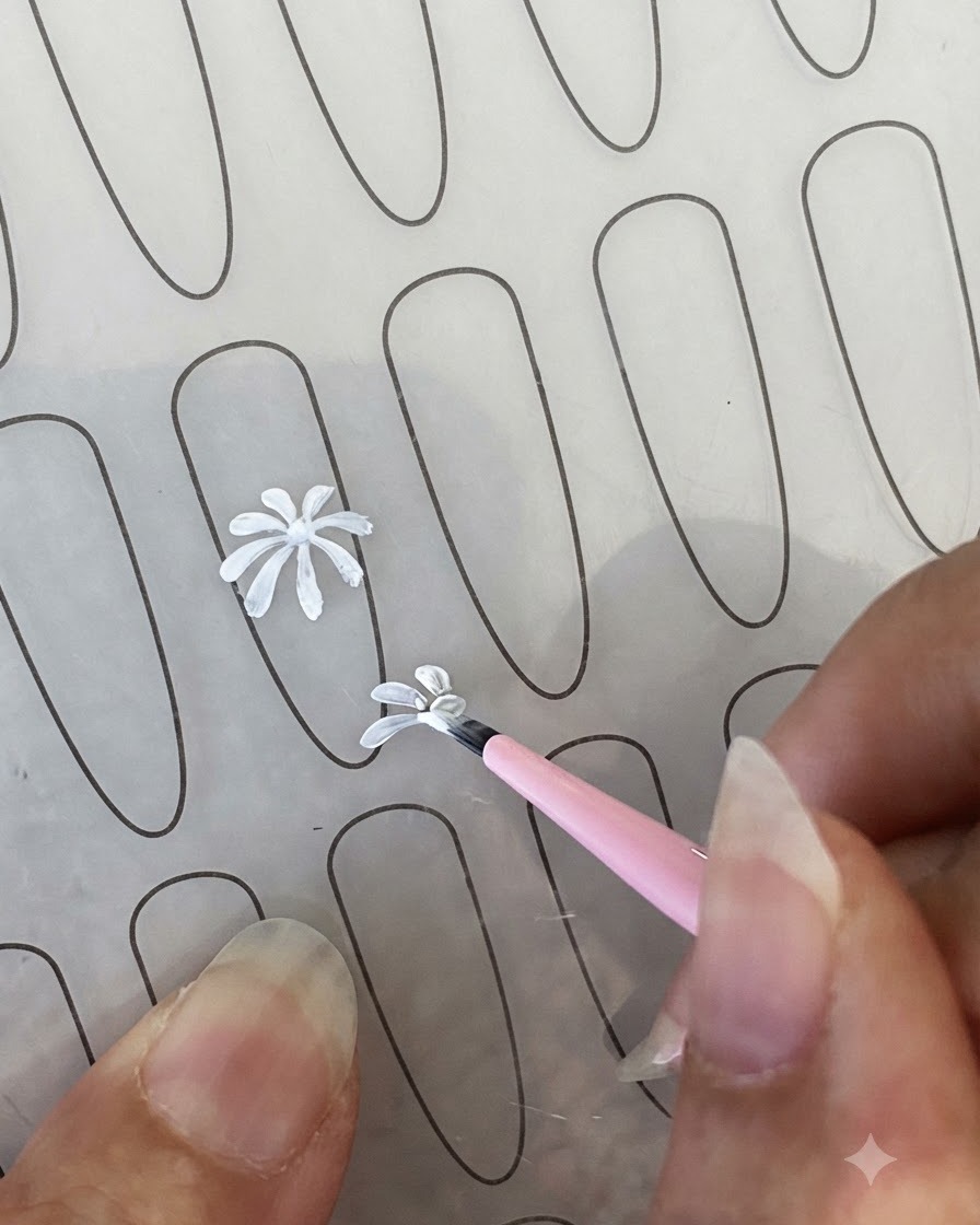 Il contorno completato di un petalo di margherita bianca su un foglio di pratica per unghie accanto a un pennello liner fine.