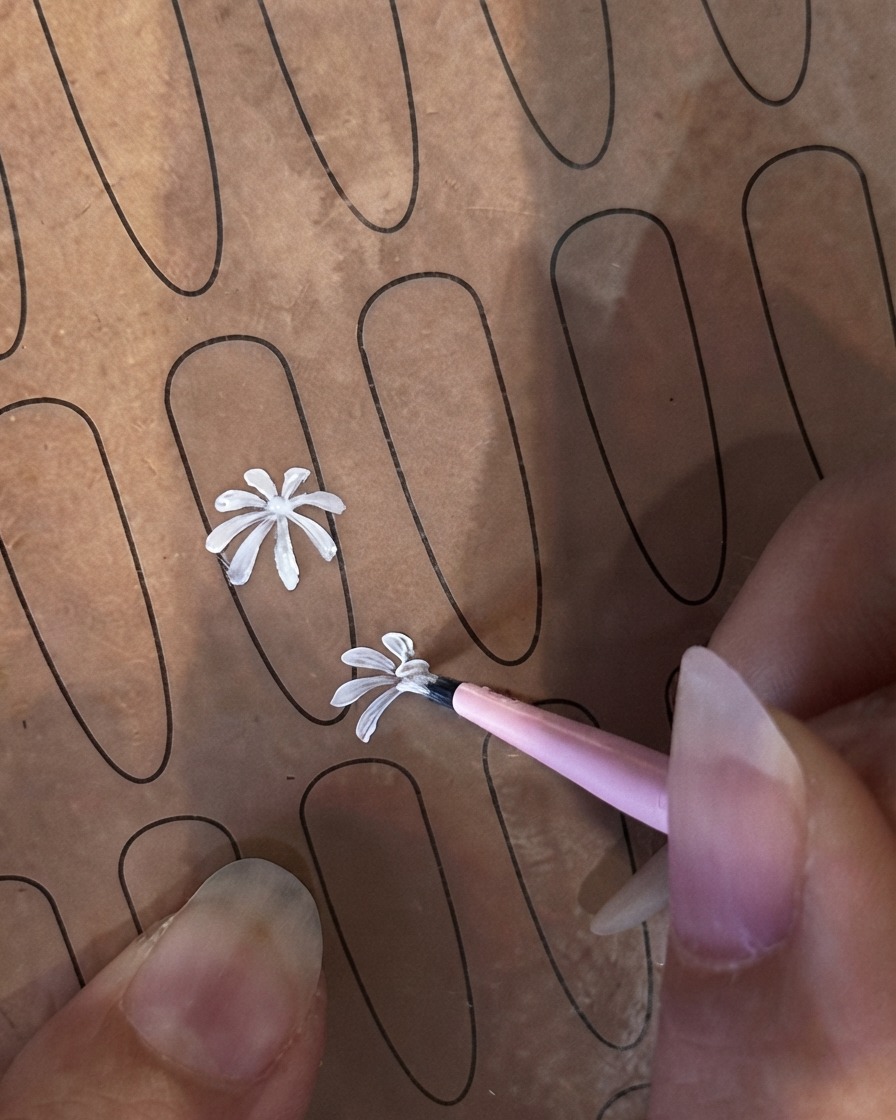 Un pennello liner fine che inizia un secondo petalo bianco più piccolo su un foglio di pratica per unghie.