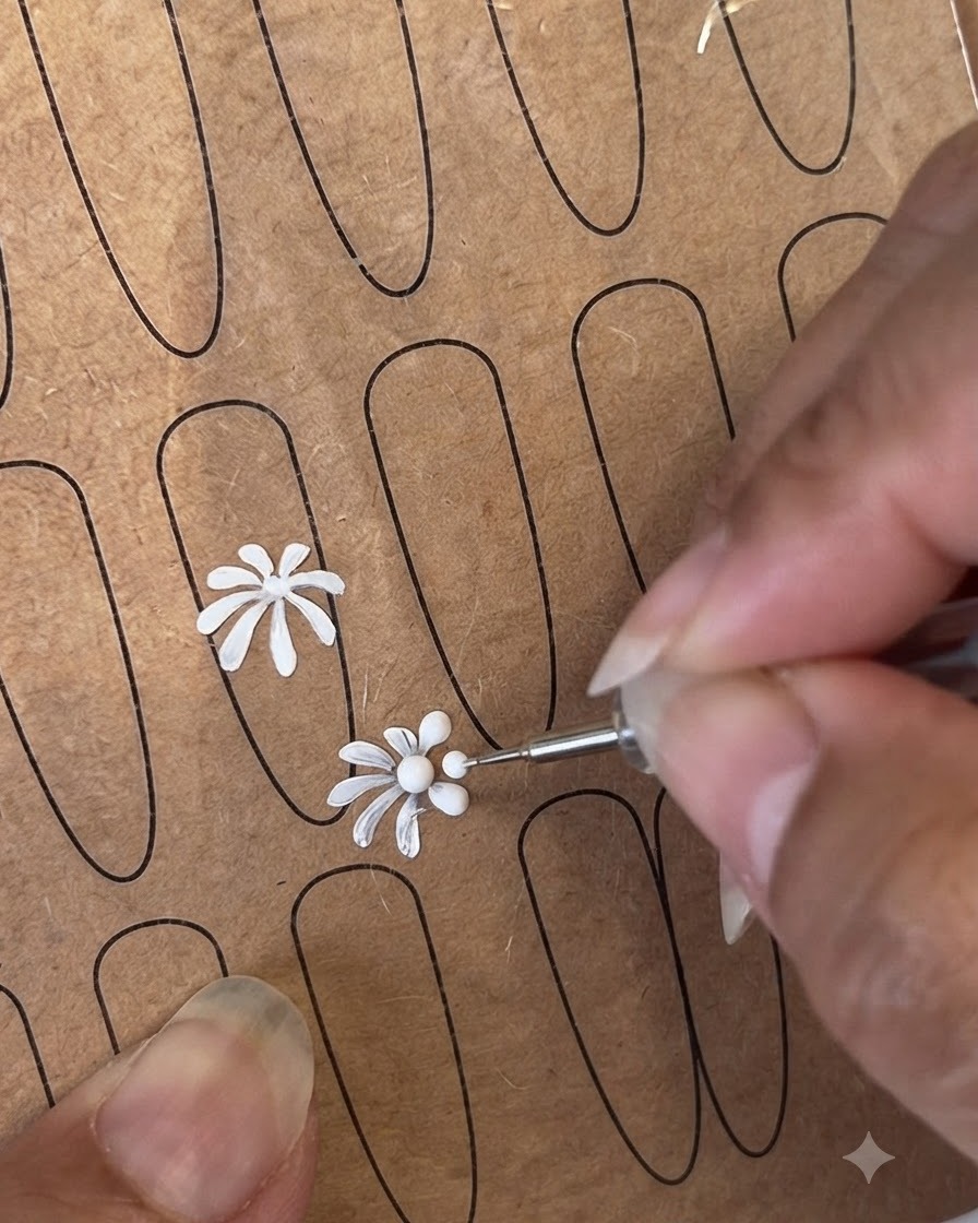 Un dotting tool e un pennello liner fine che creano centri di fiori e petali su un foglio di pratica.